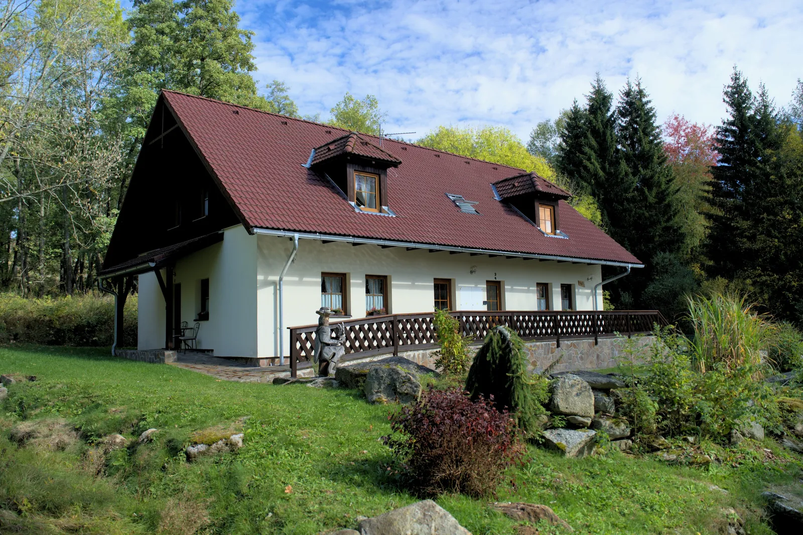Dům od louky se skalkou a dřevěnou sochou